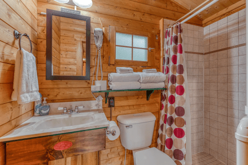 Cozy wooden bathroom featuring a shower, sink, toilet, and colorful shower curtain with towels neatly arranged.