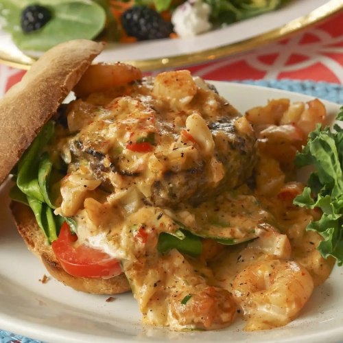 A delicious shrimp burger topped with creamy sauce, lettuce, and tomato, served on a toasted bun.