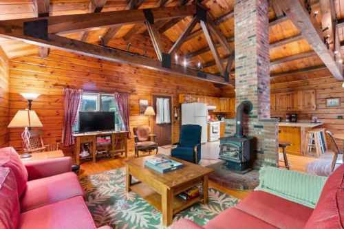 Cozy wooden cabin interior with a living area, kitchen, and rustic decor, featuring a fireplace and comfortable seating.