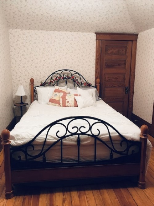 A cozy bedroom featuring a metal-framed bed with decorative pillows, a bedside lamp, and wooden accents.