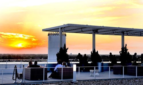 People relax on a rooftop terrace as the sun sets, casting vibrant colors across the sky.