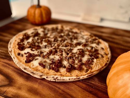 A freshly baked pizza topped with ground meat and melted cheese, placed on a wooden board with pumpkins in the background.