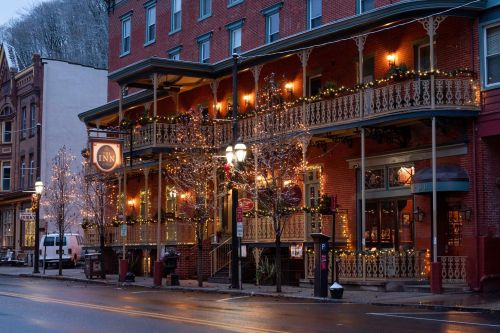 A charming inn decorated with lights and greenery, set on a quiet street during twilight.