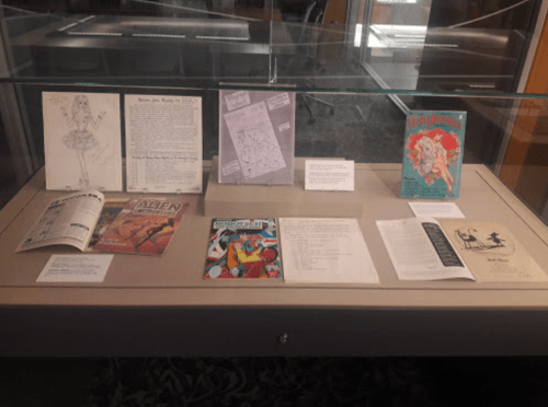 Display case featuring various comic book covers and illustrated pages, showcasing diverse artistic styles and themes.