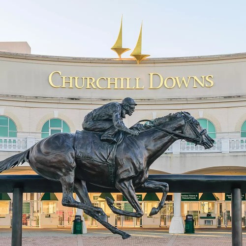 A bronze statue of a jockey riding a horse in front of the Churchill Downs entrance.