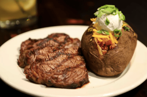 Grilled steak served with a loaded baked potato topped with cheese, bacon, green onions, and sour cream.