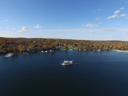 Aerial view of a serene lake surrounded by colorful autumn trees and a boat gently cruising on the water.