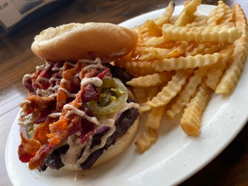 A juicy burger topped with bacon, jalapeños, and sauce, served with a side of crispy crinkle-cut fries.