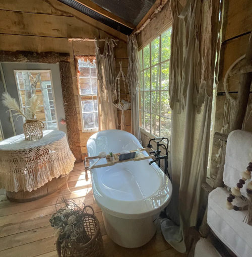 A cozy bathroom with a freestanding tub, natural light, wooden accents, and soft textiles creating a serene atmosphere.