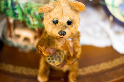 A vintage teddy bear figurine holding a small object, set against a decorative background.