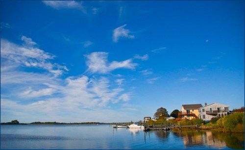 A serene waterfront scene with a clear blue sky, calm water, and a house beside a docked boat.