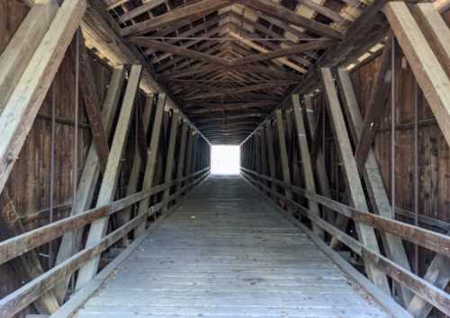 View of a wooden covered bridge interior, leading to a bright light at the end of the tunnel.