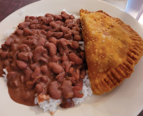 A plate featuring rice topped with red beans and a golden-brown empanada on the side.