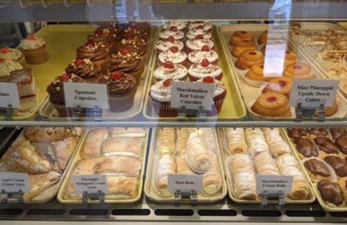 A display case filled with various cupcakes, cakes, and pastries, including red velvet and cream-filled treats.