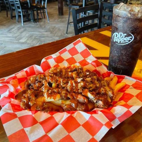 A plate of loaded fries topped with pulled pork and barbecue sauce, alongside a glass of Dr Pepper.