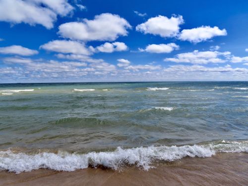 A serene beach scene with gentle waves, sandy shore, and a bright blue sky filled with fluffy clouds.