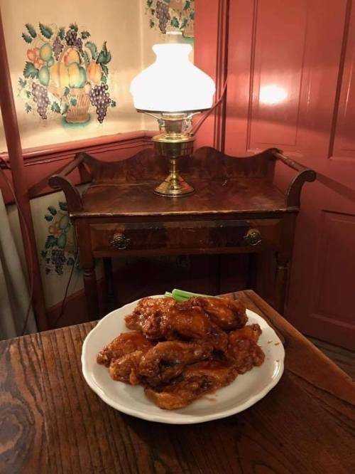A plate of glazed chicken wings sits on a wooden table beside a vintage lamp in a cozy, warmly lit room.