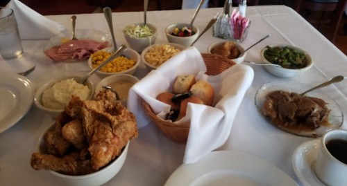 A table set with various dishes, including fried chicken, sides like mashed potatoes, corn, and salad, in bowls.