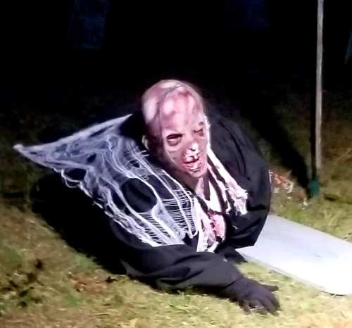 A creepy figure in a black cloak with a grotesque mask, crawling on the ground with spiderwebs around it.