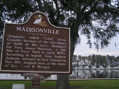 Historical marker for Madisonville, detailing its origins and significance, with a waterfront view in the background.