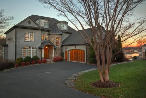 A large, elegant house with stone accents, a circular driveway, and a sunset in the background.