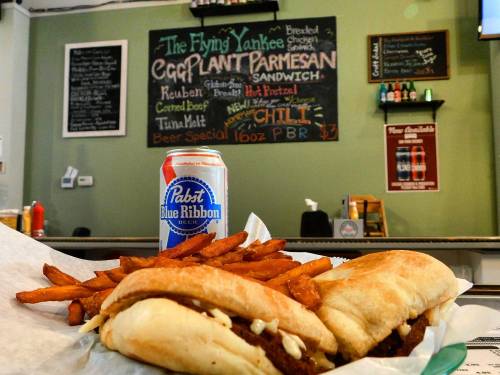 A plate with two sandwiches and sweet potato fries, alongside a can of Pabst Blue Ribbon beer on a counter.