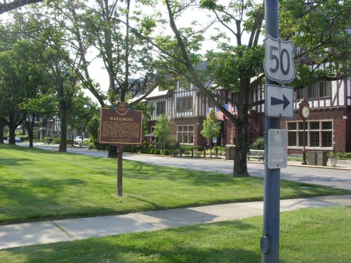 A street view of Mariemont with a historical sign, trees, and Tudor-style buildings in the background.