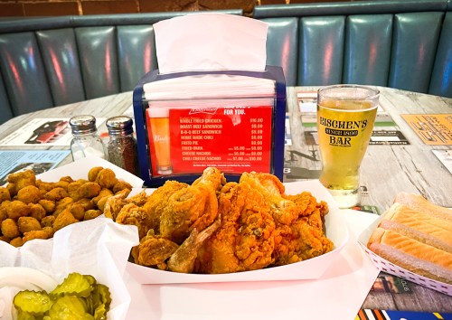 A plate of fried chicken with pickles, hushpuppies, and a glass of beer on a table with a menu holder.