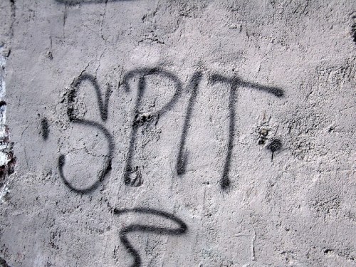 Graffiti on a textured wall featuring the word "SPIT" in bold, black spray paint.