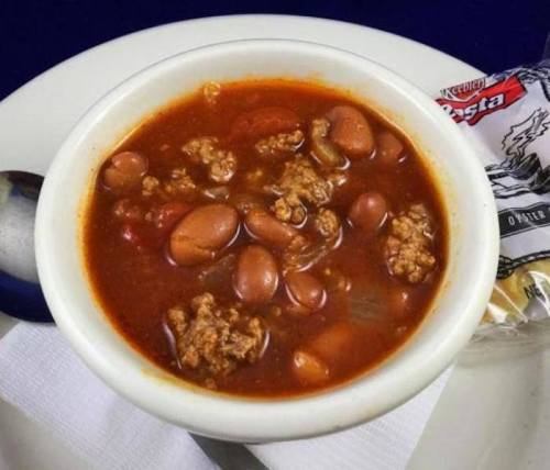 A bowl of chili with ground meat, beans, and tomatoes, served with a side of crackers on a plate.