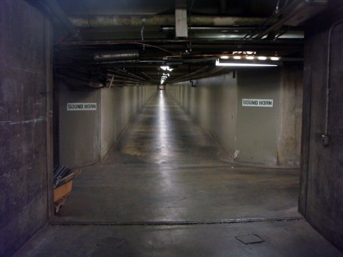 A long, dimly lit underground corridor with concrete walls and signs reading "SOUND HORN" on either side.