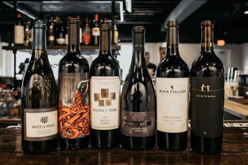 A selection of six wine bottles displayed on a bar, featuring various labels and styles.