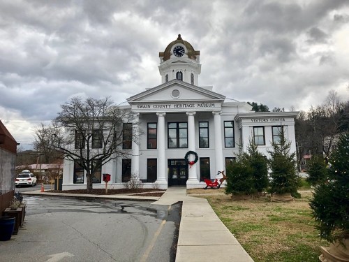 Historic Swain County Heritage Museum with a clock tower, surrounded by trees and a cloudy sky.