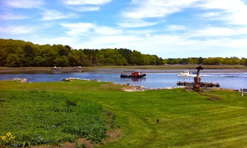 A scenic view of a river with a boat, surrounded by lush greenery and a clear blue sky.