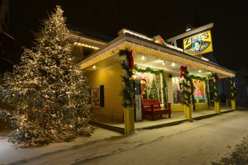 A festive store decorated with lights and wreaths, surrounded by snow and a large Christmas tree.