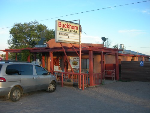 A rustic restaurant named Buckhorn, featuring a sign that reads "#7 in America," with a parking area and blue sky.