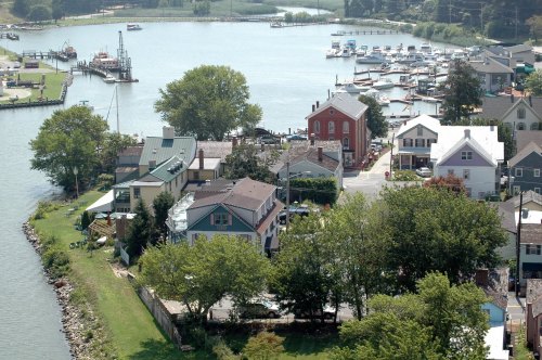 Aerial view of a scenic waterfront with houses, trees, and boats along a calm river.