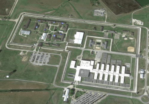 Aerial view of a large correctional facility with multiple buildings and surrounding green fields.