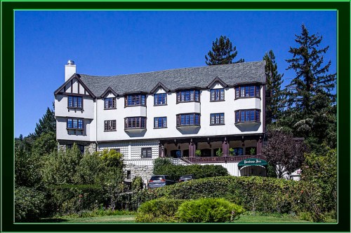 A large, elegant white building with dark trim, surrounded by trees and greenery, under a clear blue sky.
