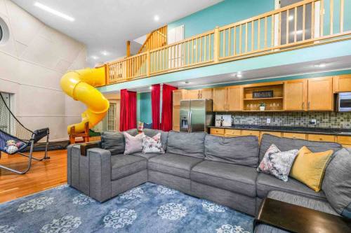 A spacious living area featuring a gray sectional sofa, kitchen, and a yellow slide leading to an upper level.
