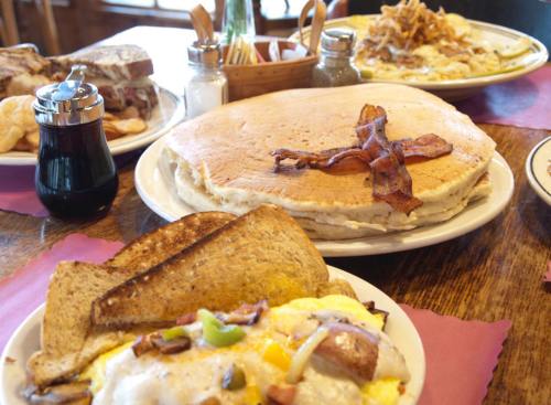 A hearty breakfast spread featuring pancakes, bacon, eggs, toast, and a side of sandwiches on a wooden table.