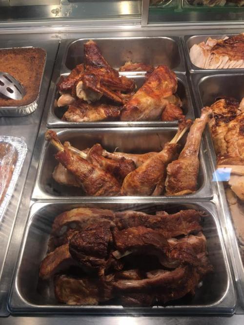 A display of various cooked meats, including turkey legs and ribs, in metal trays at a food counter.