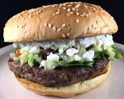 A sesame seed bun filled with a juicy beef patty, fresh vegetables, and creamy toppings on a plate.