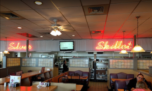 Interior of a diner with "Silver Skillet" neon sign, tables, and a view of the kitchen area in the background.