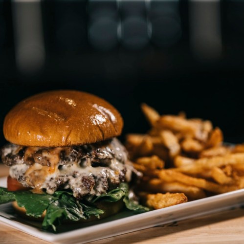 A juicy burger with melted cheese, lettuce, and tomato, served with a side of crispy fries on a white plate.