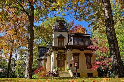 A charming historic house surrounded by vibrant autumn foliage and tall trees under a clear blue sky.