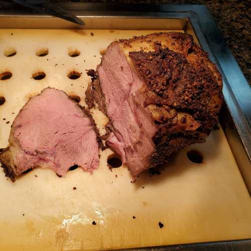 A sliced roast with a crispy exterior and pink interior, resting on a cutting board with holes.