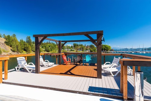 A sunny dock with colorful chairs and a shaded seating area overlooking a calm lake and marina.
