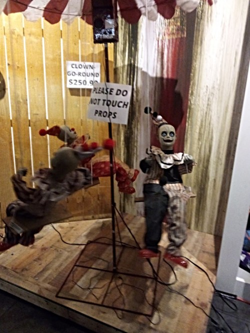 A creepy clown display with a sign saying "Please Do Not Touch Props" and a price tag for a clown-themed ride.
