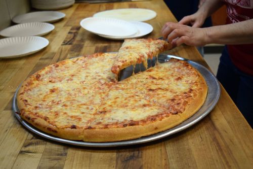 A person slices a large cheese pizza, with melted cheese stretching from the pie to a plate.